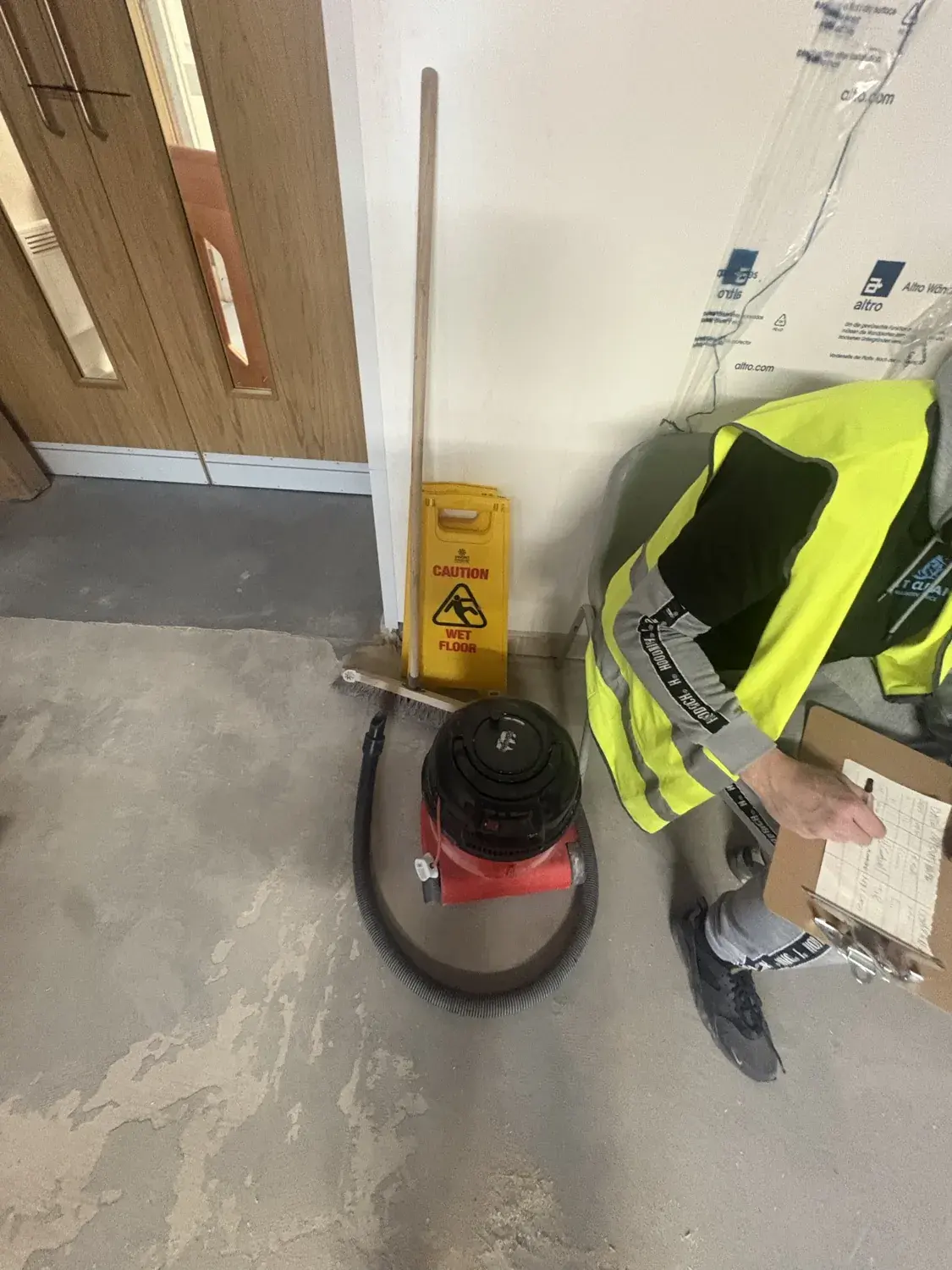 A rotary floor machine and wet floor sign in a bare corridor, paperwork being signed