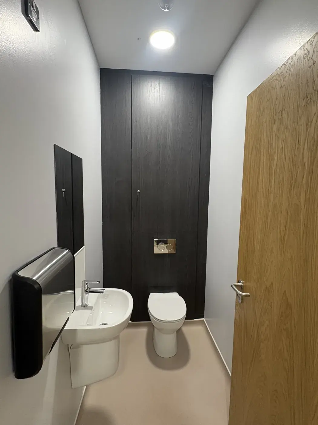 A small washroom with basin, toilet and dark panelling, wiped down and ready for use
