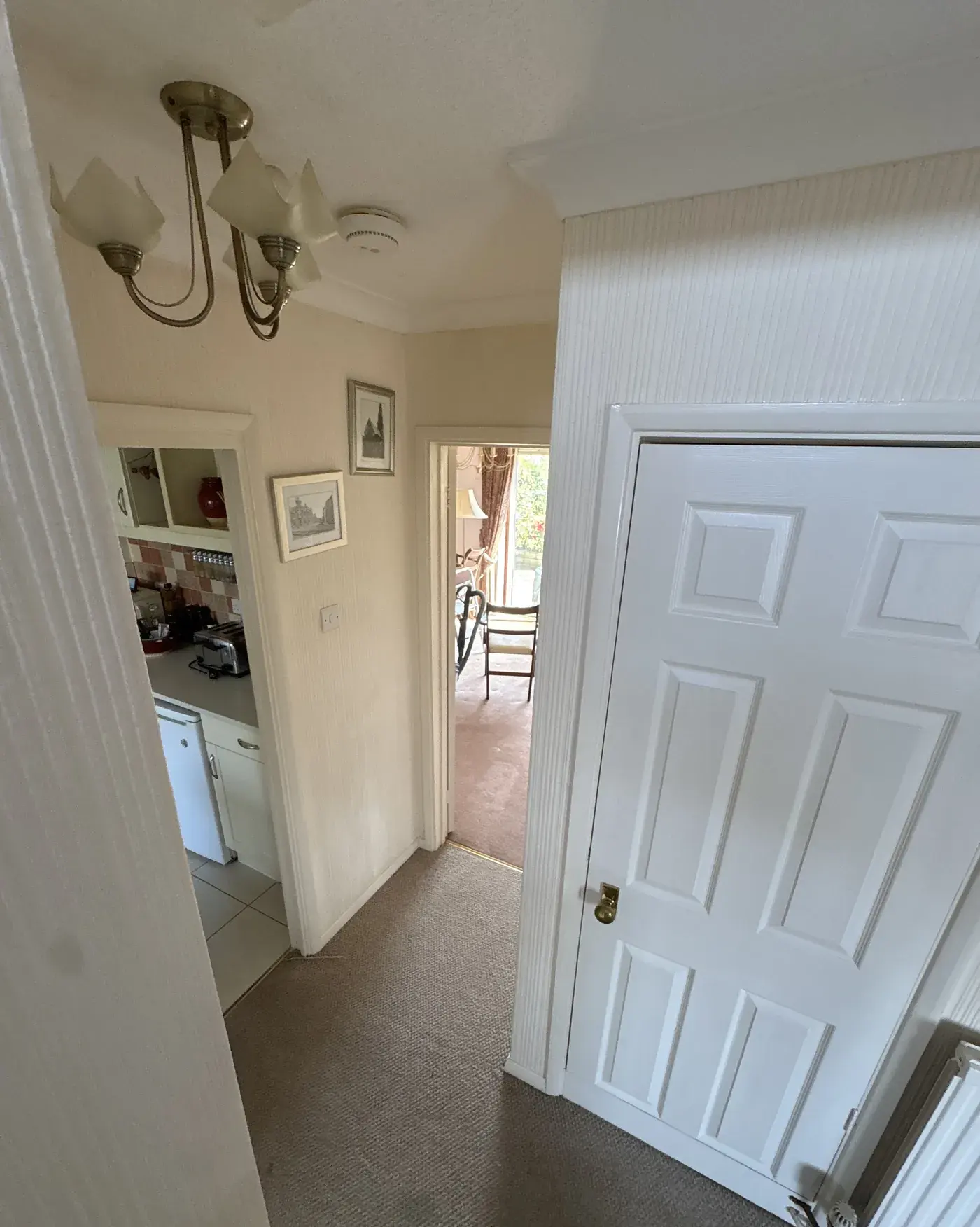 A carpeted hallway in a home, doorways open to the kitchen and dining room