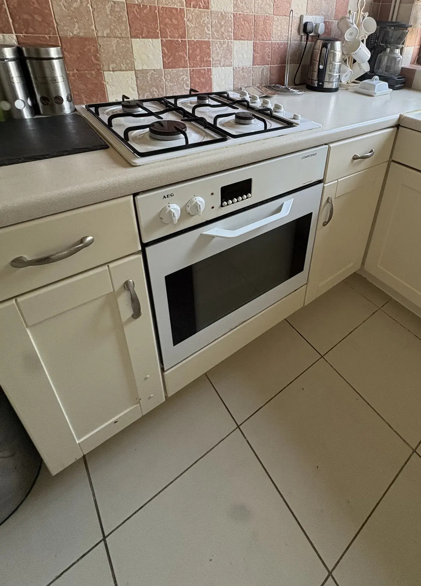 A dated cream kitchen with gas hob, built in oven and tiled floor