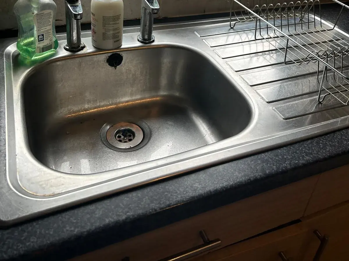 A stainless steel sink and drainer wiped down on a dark kitchen worktop
