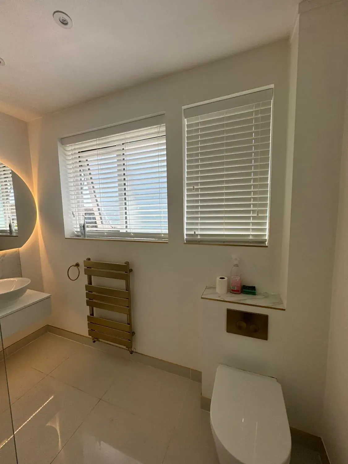 A finished bathroom with wooden blinds, brass towel rail and wall hung toilet