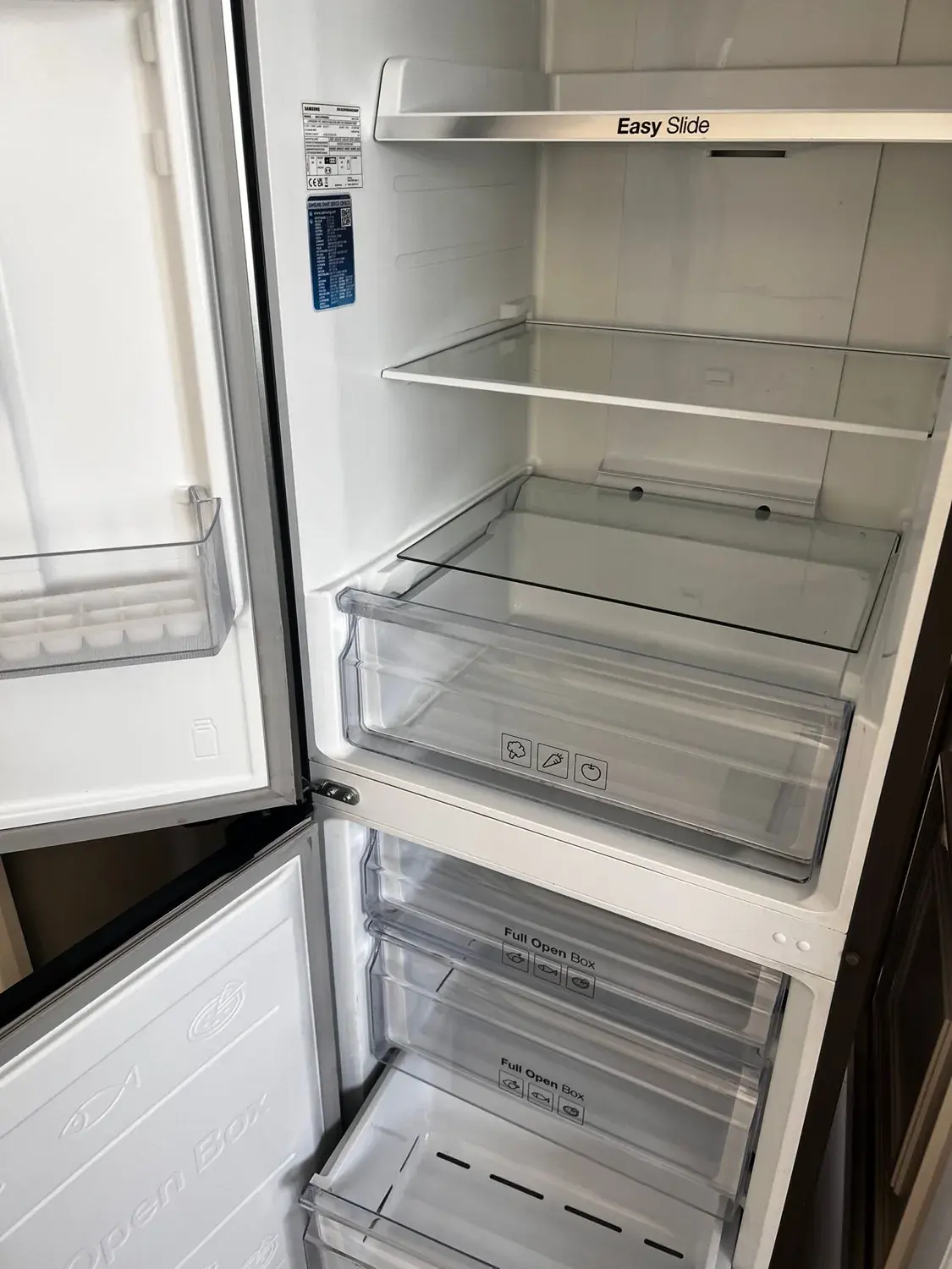 An emptied fridge freezer with both doors open, shelves and salad drawers wiped clear