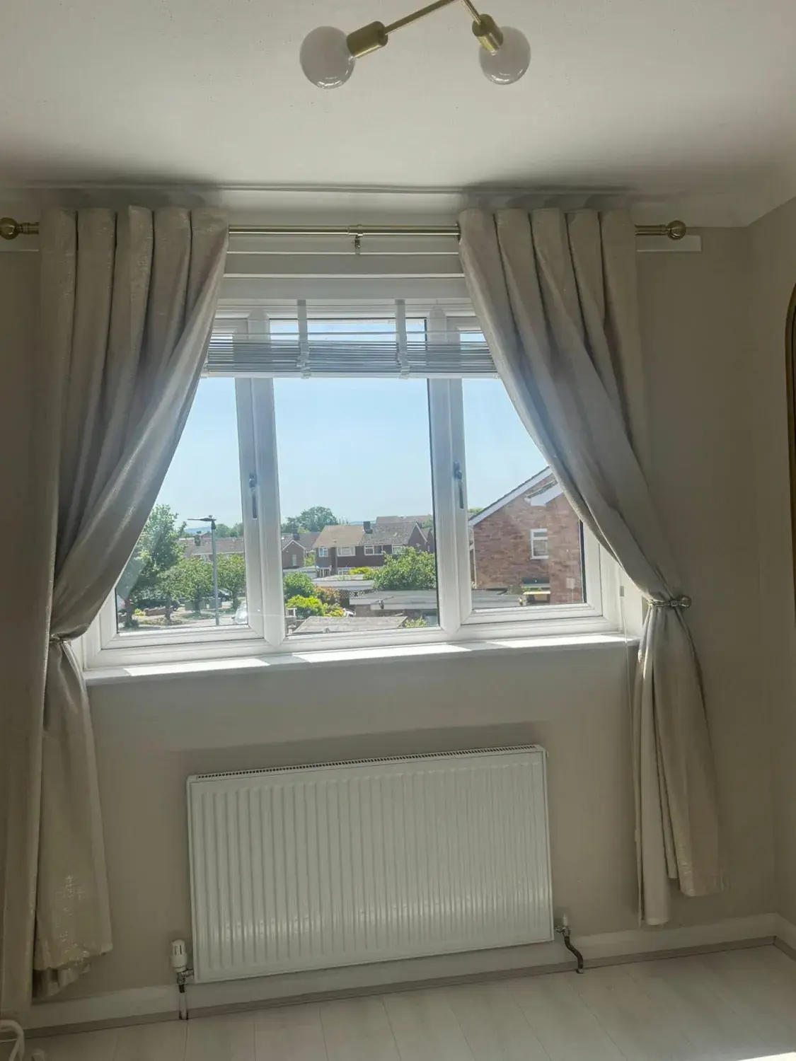 Empty bedroom with curtains, blind and radiator, window and sill cleaned inside