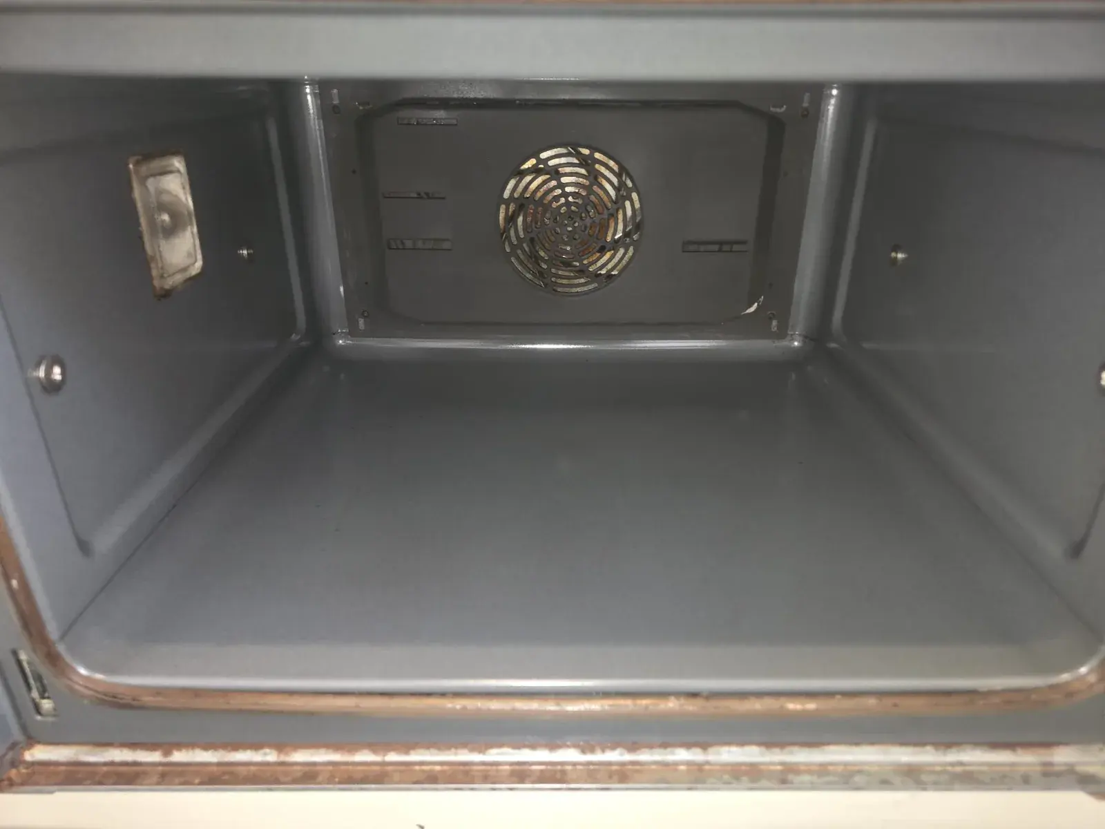 The inside of an empty oven after cleaning, bare enamel and fan cover