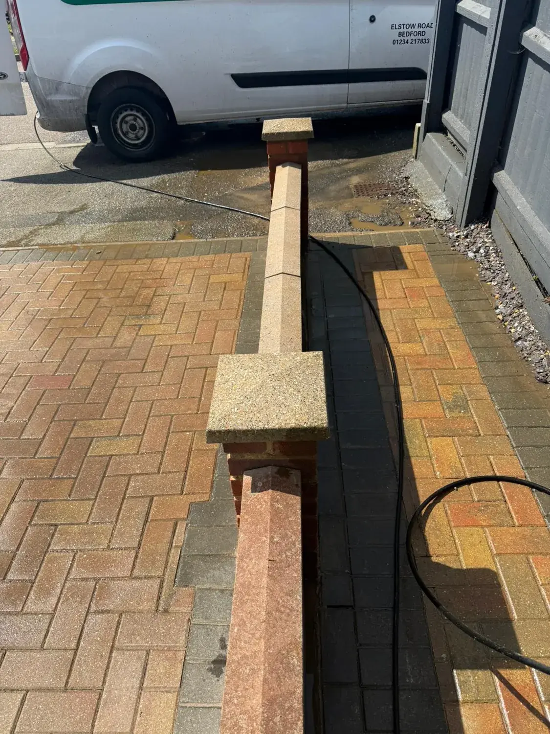 Block paving part way through a jet wash, a dark unwashed strip still running along the base of the wall