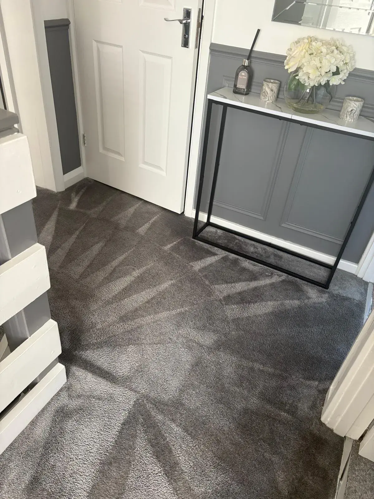 A grey hall carpet with fresh vacuum lines, console table and front door beyond