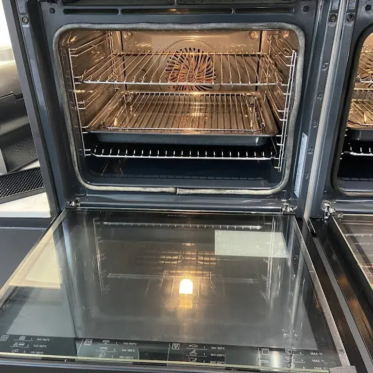 A built in double oven with the door open showing washed racks and trays